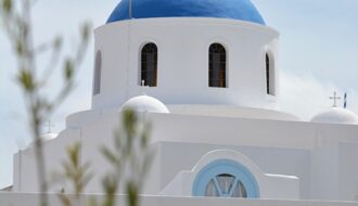 The iconic white church with a blue dome on the Greek island of Santorini overlooking the sea.