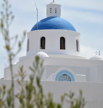 The iconic white church with a blue dome on the Greek island of Santorini overlooking the sea.