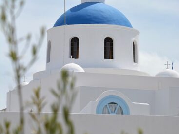 The iconic white church with a blue dome on the Greek island of Santorini overlooking the sea.