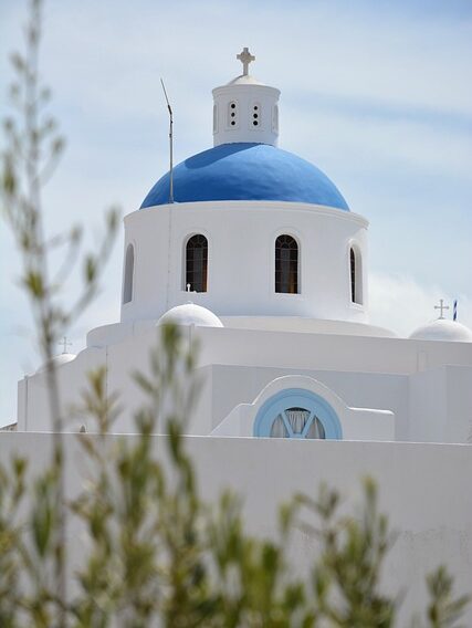 The iconic white church with a blue dome on the Greek island of Santorini overlooking the sea.